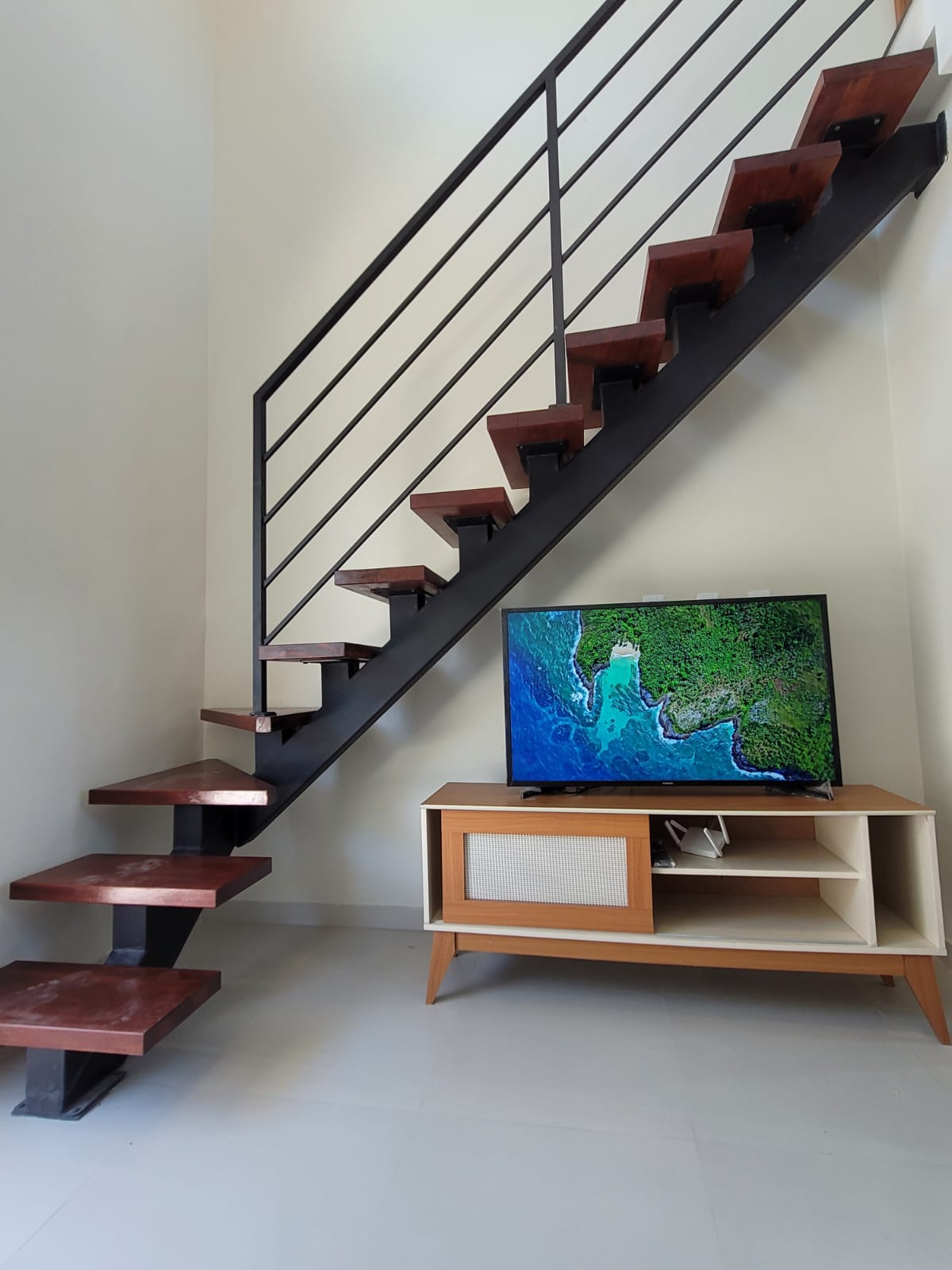 Escada de madeira com estrutura metálica preta e rack de TV com aparelho ligado